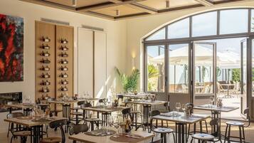 A restaurant with multiple tables and chairs, a wine rack on the wall, and a large window overlooking an outdoor area.