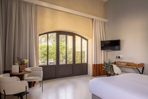 A hotel room with a bed, a desk with a chair, a TV, and a large window with curtains. - Aux Ducs De Sienne (Montagne)