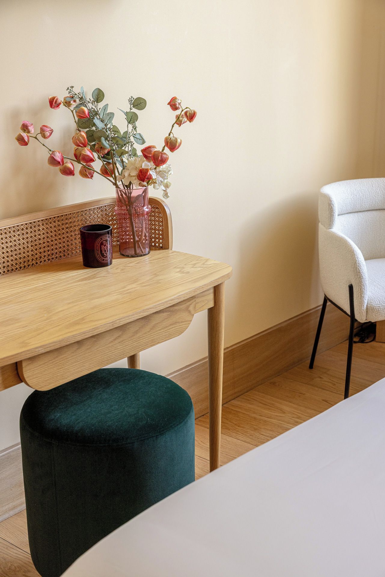 Une table en bois sur laquelle est posé un vase de fleurs, une chaise en osier et un pouf vert.
