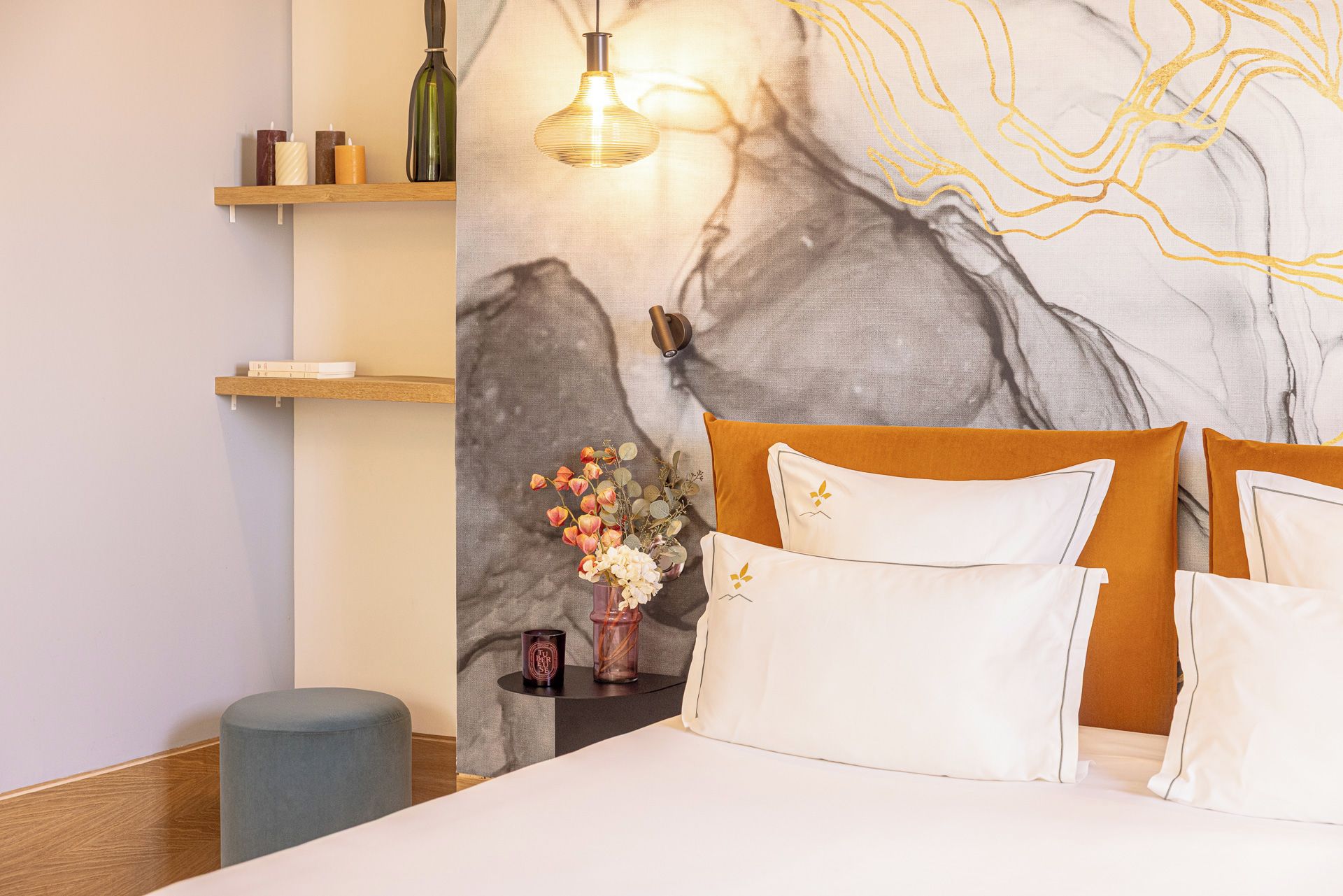 A bedroom with a bed, pillows, a nightstand, a vase with flowers, and a wall with a textured design.