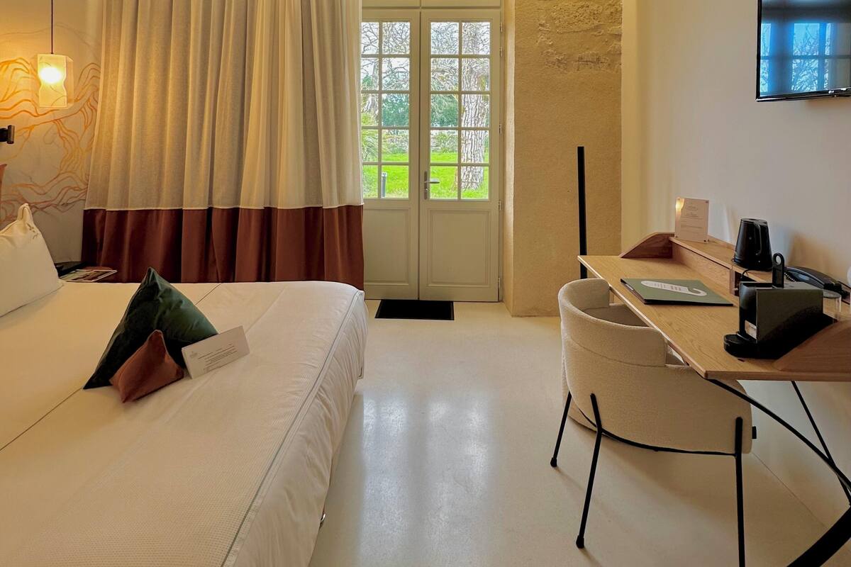 A hotel room with a bed, a desk, a chair, a TV, and a window with curtains.