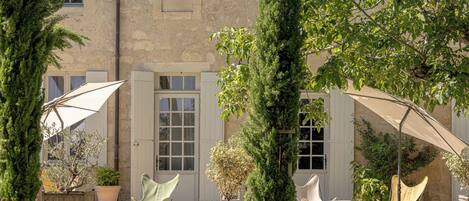 A courtyard with outdoor seating, a stone wall, and a building with windows and a door.
