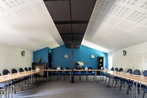 Un salón de conferencias con una mesa larga, sillas y una pared azul decorativa.