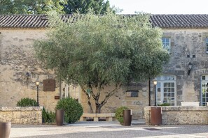 A stone building with a tiled roof, a bench, and a tree in front. - Aux Ducs De Sienne (Montagne)