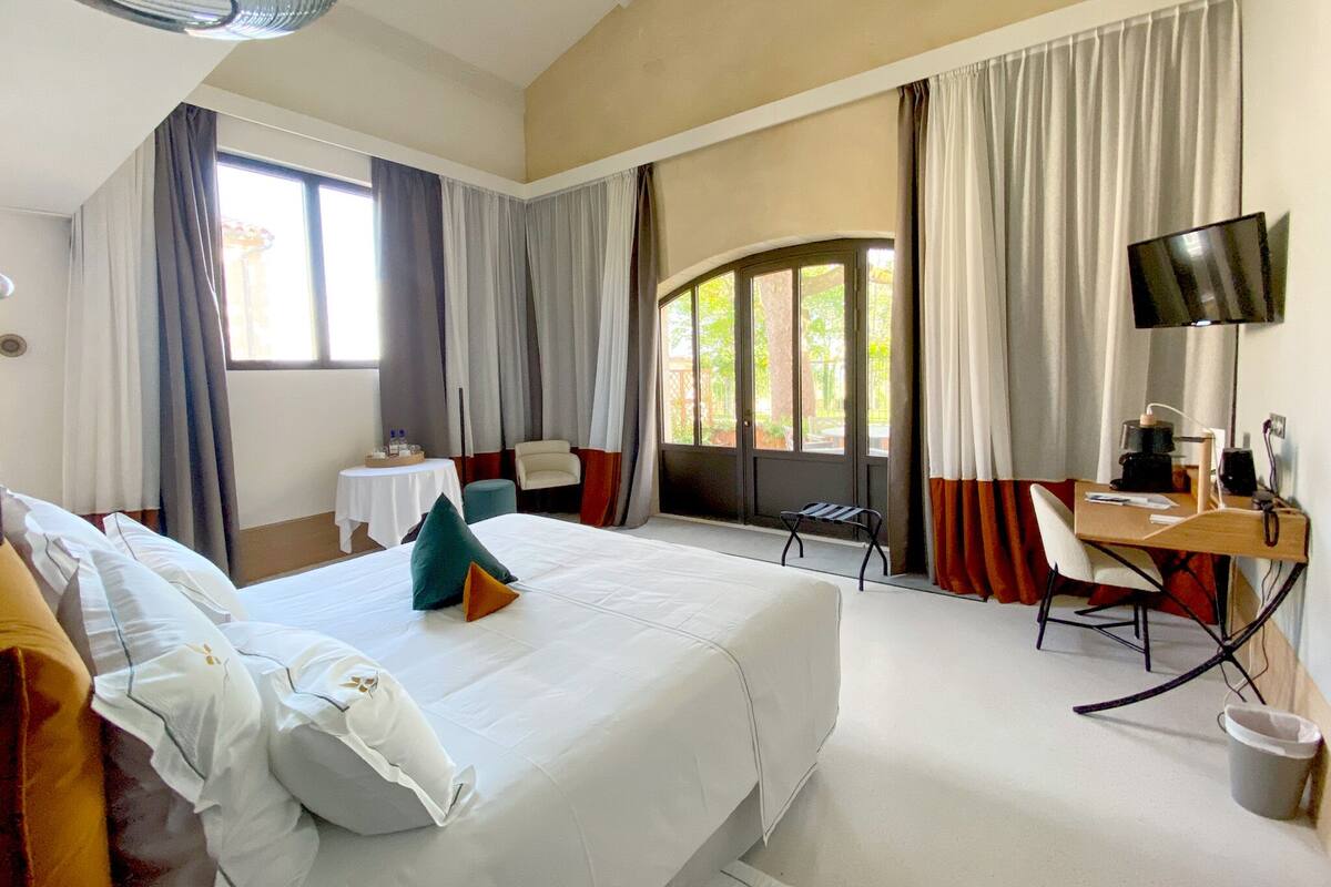 A hotel room with a large bed, a desk, a chair, a TV, and a window with curtains.