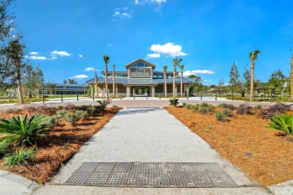 A modern building with a central entrance, surrounded by landscaped areas with pine and palm trees.