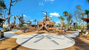 Un parque infantil con un tobogán central, rodeado por una zona pavimentada circular y una plataforma de madera.