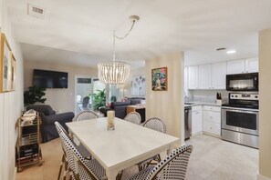 A modern kitchen with white cabinets, a stainless steel oven, and a dining area with a white table and patterned chairs.