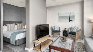 A modern hotel room with a bed, TV, wicker chairs, and a coffee table. - Modern And Trendy 1 Bed Across From Rosebank Mall (Johannesburg)
