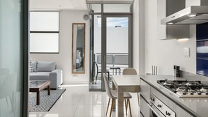 A modern kitchen with a gas stove, a dining area with a table and chairs, and a living area with a sofa and a coffee table. - Modern And Trendy 1 Bed Across From Rosebank Mall (Johannesburg)
