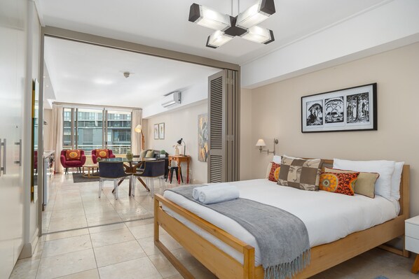 A modern hotel room with a large bed, a desk, and a seating area with chairs.
