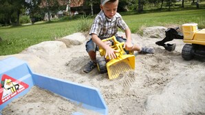 Et barn leger med sand og legetøjsbiler udendørs.