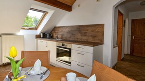 Spisestue med et bord dækket til to, et køkken med moderne hårde hvidevarer, og et ovenlys over bordet.