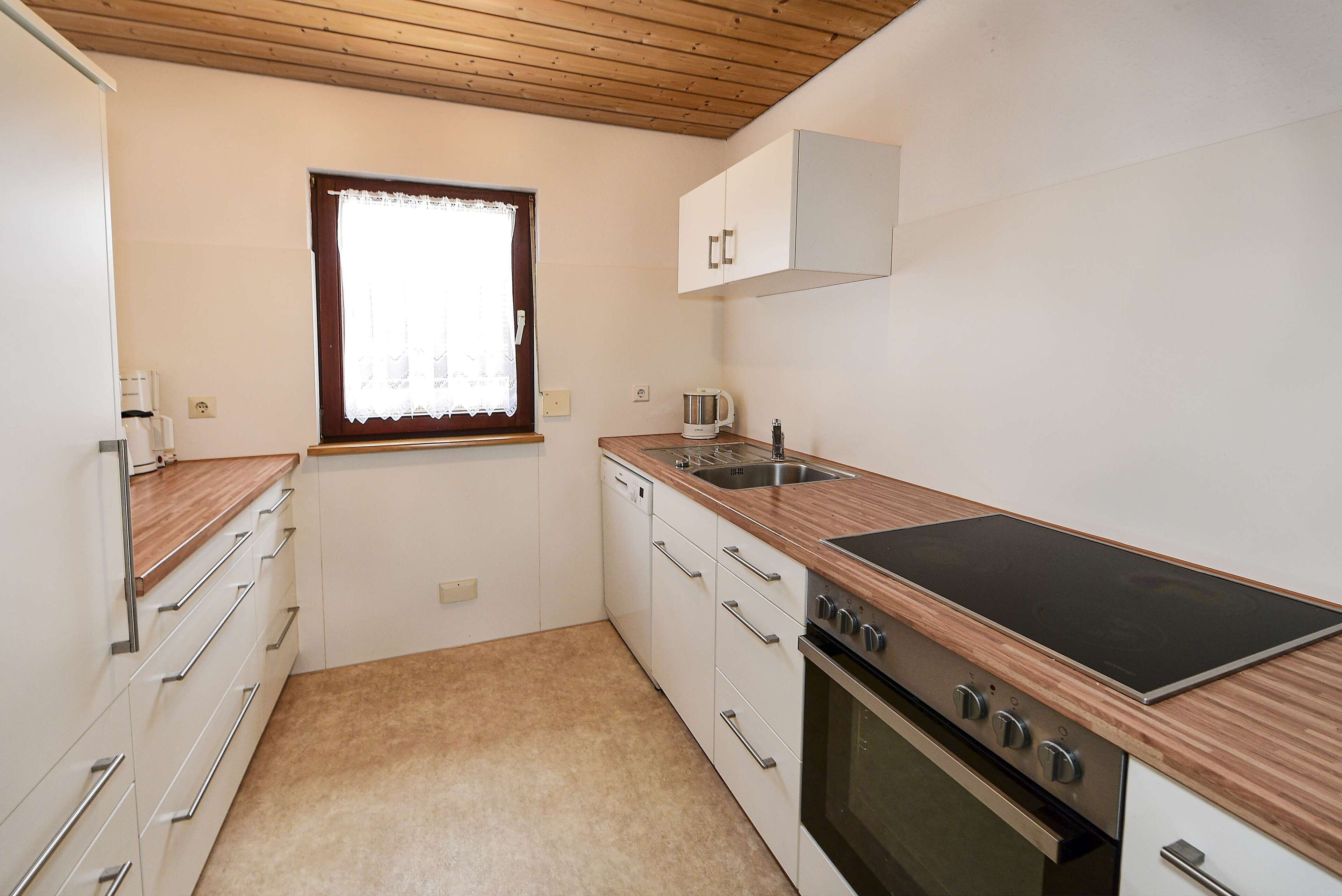 A compact kitchen with a built-in stove, a sink, and a window with a lace curtain.