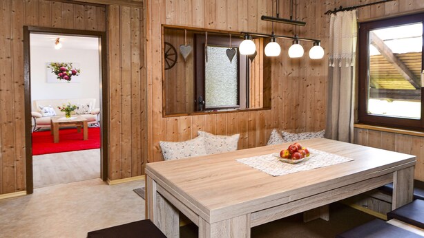 Una stanza con rivestimento in legno, un tavolo da pranzo, una finestra con vista e un tappeto rosso che conduce a una zona con divano.