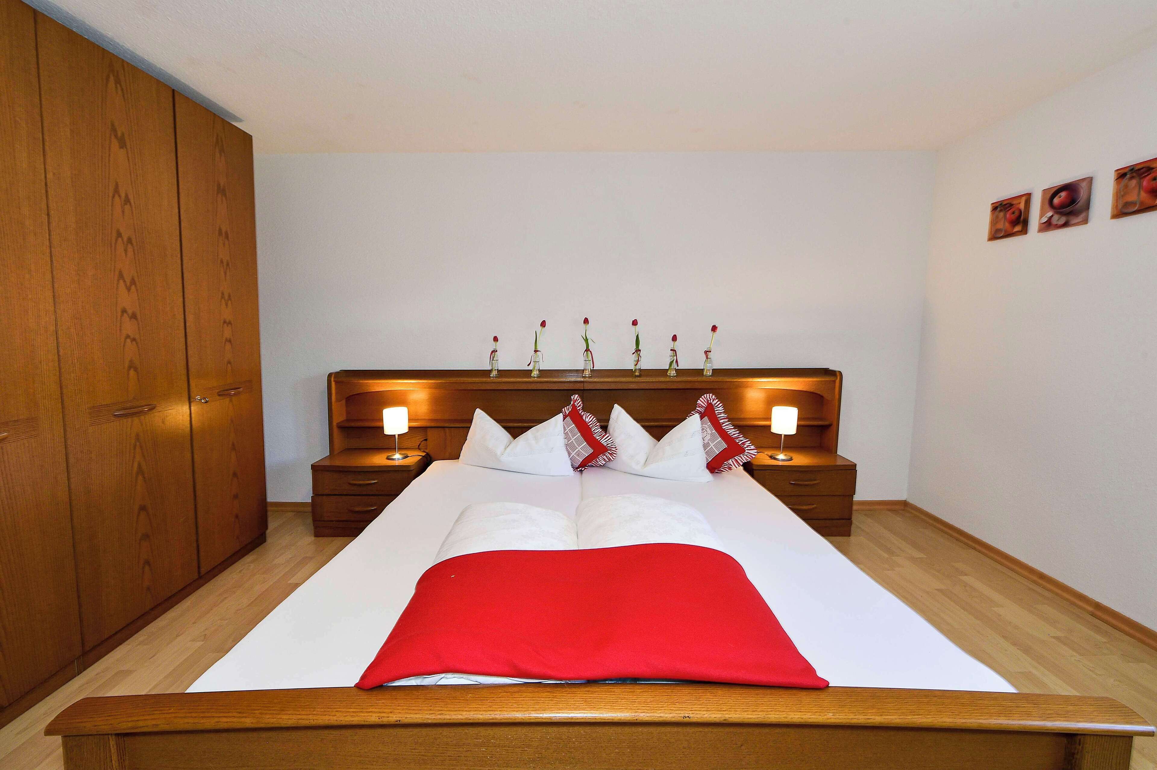 Un lit bien fait, avec une couverture rouge, une tête de lit en bois et des lampes de chevet.