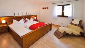 Una camera da letto con un letto di legno, un comodino, una finestra con tende e una poltrona con una coperta di pelliccia.
