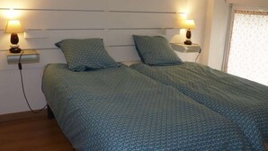 A double bed with a patterned duvet, bedside lamps, and a window with a patterned curtain. - Aux Pierres de Noziières  (Gramat)