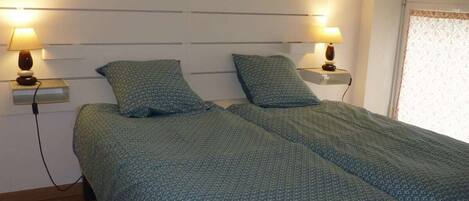 Una cama doble con un edredón estampado, lámparas de noche y una ventana con cortina decorada.