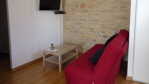 A room with a red sofa, a small wooden table, and a TV mounted on a white wall. - Aux Pierres de Noziières  (Gramat)