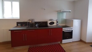 A compact kitchen with a red countertop, a microwave, a coffee maker, a stove, and a refrigerator. - Aux Pierres de Noziières  (Gramat)