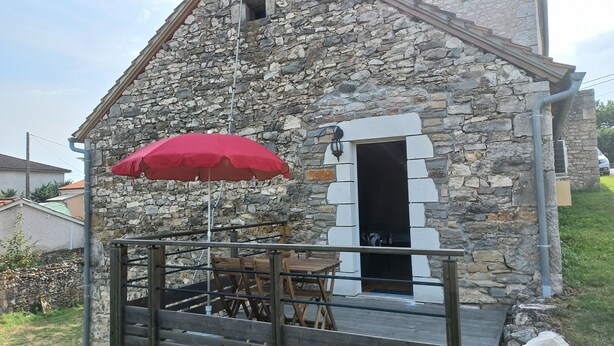 A stone building with a wooden deck, a red umbrella, and a door. - Aux Pierres de Noziières  (Gramat)
