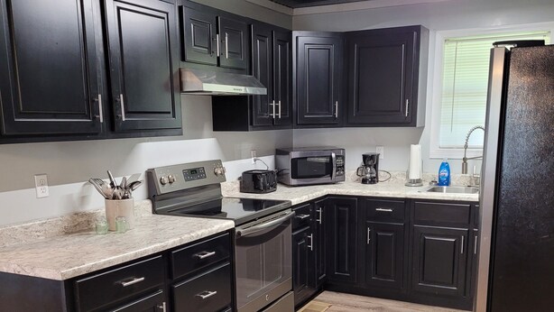A modern kitchen with dark cabinetry, stainless steel appliances, and a granite countertop.