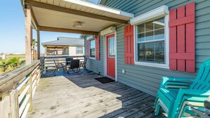 Une terrasse couverte, aménagée avec du mobilier d’extérieur, dotée d’une rambarde en bois, et une maison avec des volets rouges.