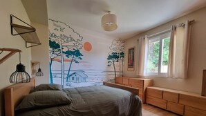 A bedroom with a bed, wooden headboard, bedside tables, a window with curtains, and a wall mural. - Villa 5 Piéces Avec Piscine (Le Porge)
