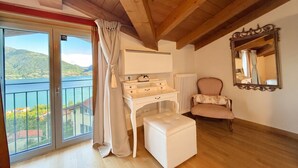 Quarto com varanda, cômoda branca, cadeira listrada e espelho na parede.