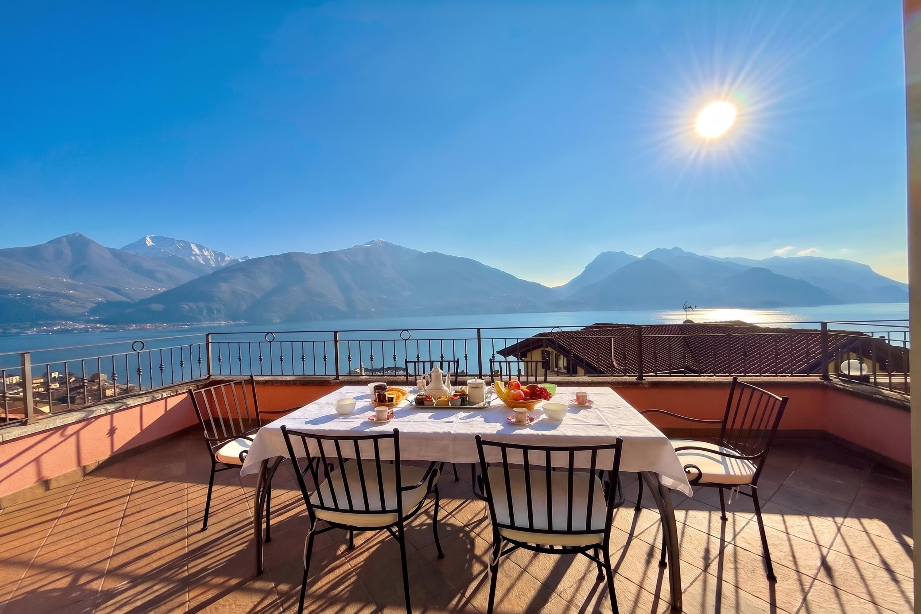 A terrace with a table set for two, overlooking a lake and mountains.