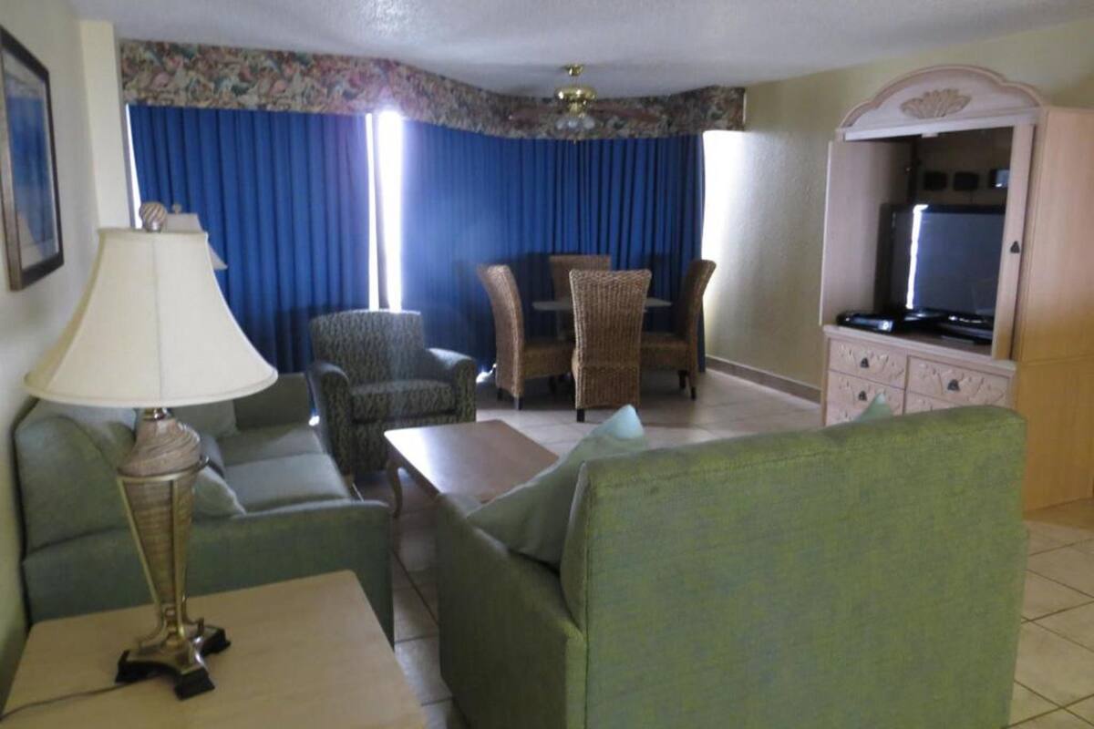 A living room with a sofa, armchairs, a coffee table, a lamp, a television, and a cabinet.