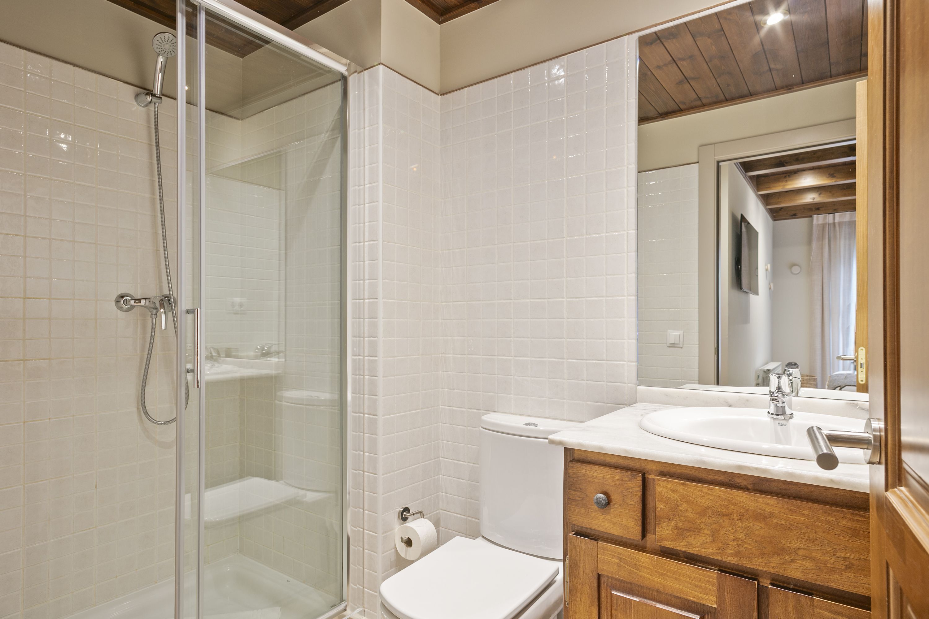 Un baño con cabina de ducha de vidrio, un inodoro blanco y un tocador de madera con lavamanos.