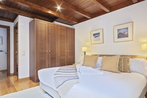 A bedroom with a wooden wardrobe, a bed with multiple pillows, and two framed pictures on the wall. - Luderna - Apartamento Val de Ruda B14 Paulet (Baqueira)