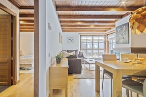 A modern living room with a wooden ceiling, a sofa, a dining table with chairs, and a large window with a view. - Luderna - Apartamento Val de Ruda B14 Paulet (Baqueira)
