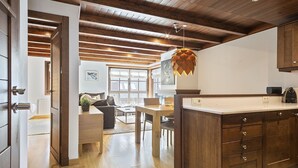 A modern kitchen with wooden cabinets, a dining area with a table and chairs, and a cozy living space with a sofa and a fireplace. - Luderna - Apartamento Val de Ruda B14 Paulet (Baqueira)