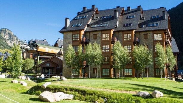 A multi-story hotel with a stone facade, multiple balconies, and a well-maintained lawn with large rocks. - Luderna - Apartamento Val de Ruda B14 Paulet (Baqueira)