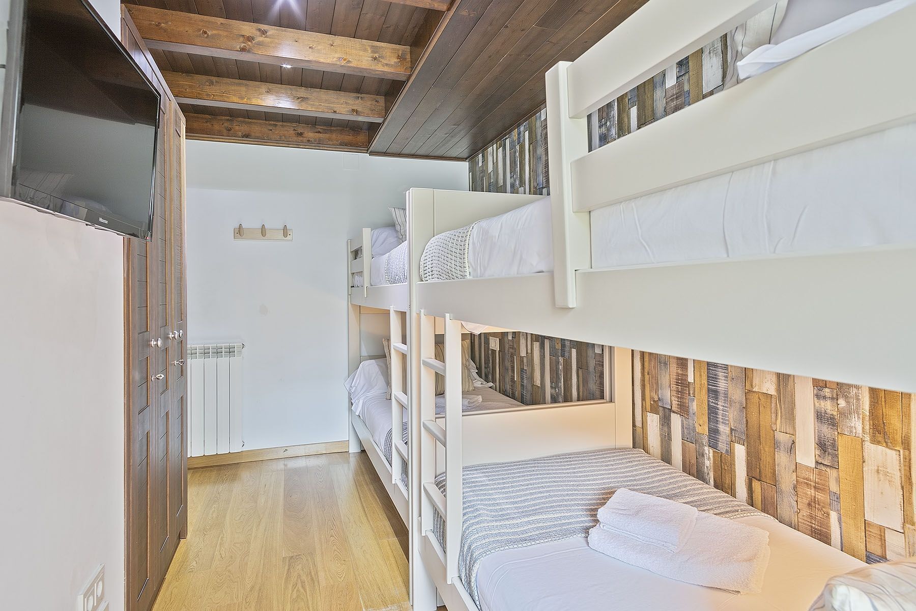A bunk bed room with a wooden ceiling, a radiator, and a wooden wall panel.