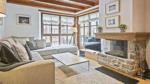A cozy living room with a stone fireplace, large windows, and a modern sofa. - Luderna - Apartamento Val de Ruda B15 Baretja (Baqueira)