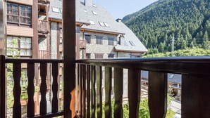 A wooden balcony with a stone building in the background, surrounded by a forested mountain. - Luderna - Apartamento Val de Ruda B15 Baretja (Baqueira)