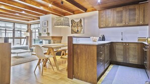 A modern kitchen with wooden cabinets, a dining area with a table and chairs, and a large window providing natural light. - Luderna - Apartamento Val de Ruda B15 Baretja (Baqueira)