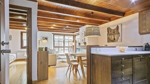 A modern kitchen with wooden cabinets, a dining area with a table and chairs, and a large window providing natural light. - Luderna - Apartamento Val de Ruda B15 Baretja (Baqueira)
