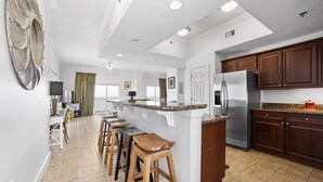 A modern kitchen with a central island, wooden bar stools, and dark wooden cabinets. - Seawind 300 by Liquid Life (Gulf Shores)