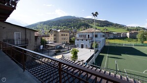 Udsigt fra en balkon over en tennisbane, med bygninger og et bjerg i baggrunden.