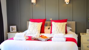 Una cama bien hecha con ropa de cama roja y blanca, una bandeja de fruta y toallas en una habitación de hotel.