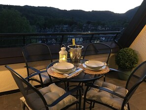 Mesa posta para dois em uma varanda com vista para uma vila na encosta.