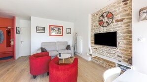 Un salon moderne avec un mur en pierre, un téléviseur à écran plat, un canapé gris, des fauteuils rouges et une table basse blanche.