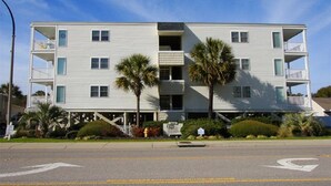 A multi-story building with balconies, palm trees, and a clear sky.