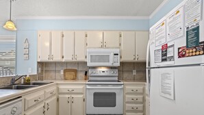A kitchen with white cabinets, a microwave, an oven, and a refrigerator. There are wall-mounted papers and a hanging light fixture.