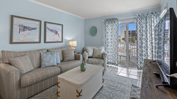 A living room with a sofa, a coffee table, a chair, and a TV. There are two framed pictures on the wall.
